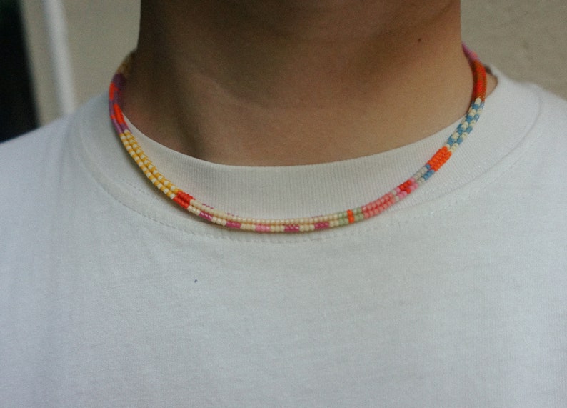 May include: A colorful beaded necklace with a repeating pattern of orange, yellow, pink, and blue beads. The necklace is worn around the neck and is against a white background.