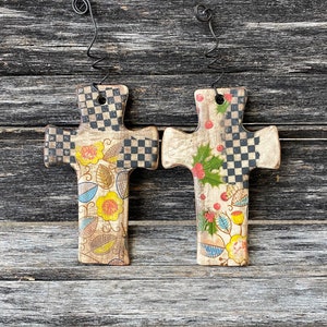 May include: Two wooden cross ornaments with a black and white checkered pattern and floral designs. The crosses are painted with yellow, red, green, and blue flowers.