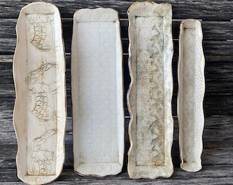 May include: Four white ceramic serving dishes with different embossed patterns. The dishes are arranged in a row on a wooden surface.