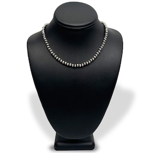 May include: A silver beaded necklace on a black display stand. The necklace is made of small, round beads.