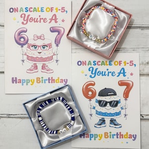 May include: Two birthday cards with cake characters holding balloons that read "6" and "7", and the text "Happy Birthday". Two bracelets are in gift boxes. One bracelet is colorful, the other is blue and white.