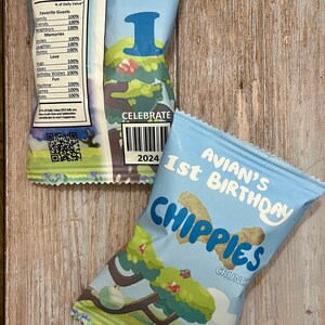 May include: A blue and white bag of cheese flavored snacks with the text "Avian's 1st Birthday Chippies Crunch" and a cartoon tree on the front. The back of the bag has a nutrition facts label with the text "Guaranteed Fun Birthday Nutrition Facts".
