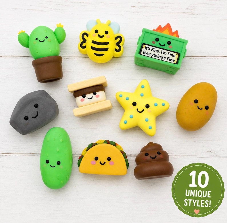 May include: A collection of ten small, colorful erasers featuring various characters and objects, including a green cactus, a yellow bee, a green dumpster with the text It's Fine, I'm Fine Everything's Fine, a gray rock, a s'more, a yellow star, a potato, a green pickle, a taco, and a brown swirl.