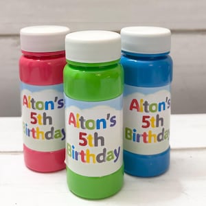 May include: Three colorful bubble bottles: pink, green, and blue. Each bottle has a white cap and a label that reads "Alton's 5th Birthday" in colorful letters. The bottles are cylindrical and filled with bubble solution.