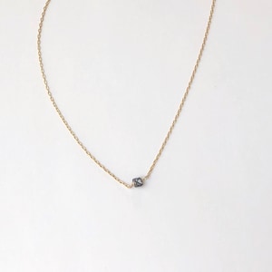 Puede incluir: Un delicado collar de cadena dorada con un pequeño colgante de piedra preciosa azul oscuro.