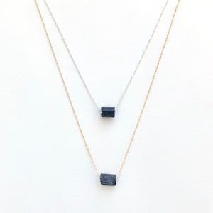 May include: Two delicate necklaces with small, dark blue rectangular gemstones. One necklace has a silver chain, and the other has a gold chain. The gemstones appear to be raw or unpolished, adding a natural element to the jewelry.