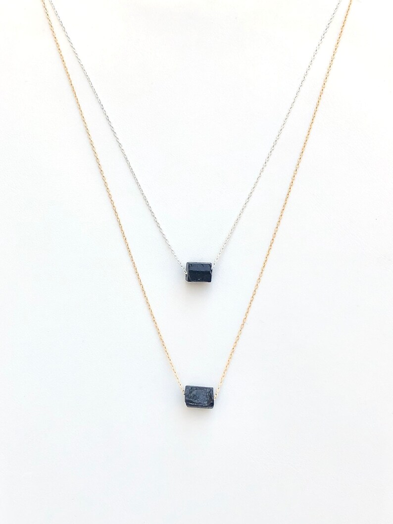 May include: Two delicate necklaces with small, dark blue rectangular gemstones. One necklace has a silver chain, and the other has a gold chain. The gemstones appear to be raw or unpolished, adding a natural element to the jewelry.