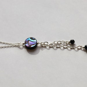 May include: A silver chain necklace with a round iridescent abalone shell pendant and two black beads dangling from the chain.