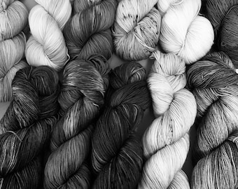 May include: A collection of skeins of yarn in various shades of gray and white. The yarn is arranged in a pattern of alternating colors.