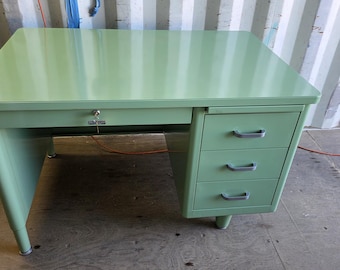 May include: A vintage mint green metal desk with a rectangular top, a single drawer with a key, and a three-drawer cabinet. The desk has a streamlined design with curved legs and silver-toned drawer pulls. The desk measures approximately 48 inches wide and 30 inches deep.