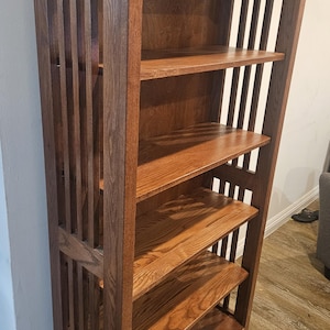 May include: A wooden bookshelf with a dark brown finish. The bookshelf has five shelves and vertical slats on the sides. The shelves are made of wood and are a lighter shade of brown. The bookshelf is sturdy and well-crafted.