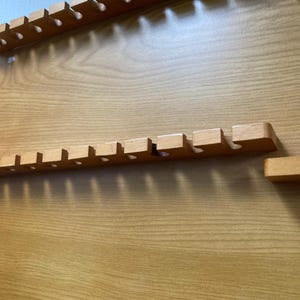May include: A wooden wall-mounted organizer with multiple slots for storing items. The organizer has a light brown wood finish and is made of solid wood.