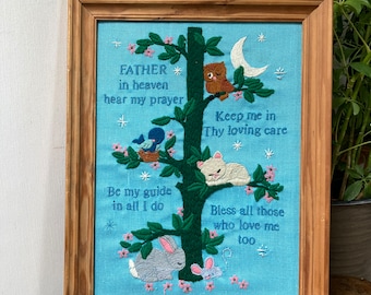 May include: Embroidered wall art with a blue background and a tree with animals. The text reads "Father in heaven hear my prayer, Keep me in Thy loving care, Be my guide in all I do, Bless all those who love me too."