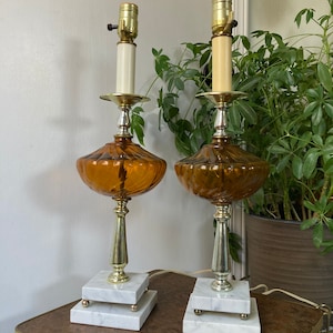 May include: A pair of amber glass table lamps with white marble bases. The lamps have a fluted design and a silver-tone finish.