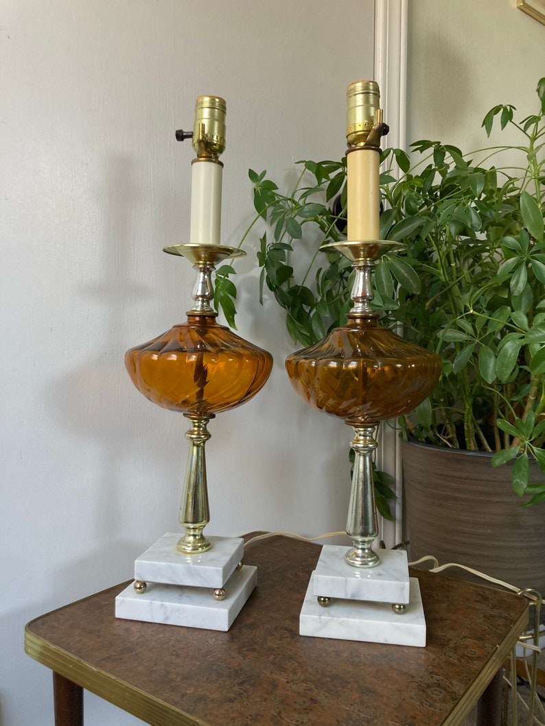 May include: A pair of amber glass table lamps with white marble bases. The lamps have a fluted design and a silver-tone finish.