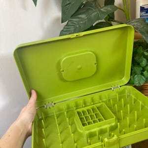 May include: Open, lime green dish drying rack with a lid. The rack has a rectangular shape with a raised center section and vertical pegs for holding dishes. The lid is open, revealing the interior. The rack is made of plastic.