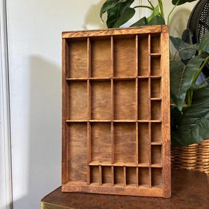 May include: A rectangular wooden printer's tray featuring a natural brown finish and multiple internal compartments of varying sizes. The organizer is constructed with thin wooden dividers that create a grid of open slots for storage.