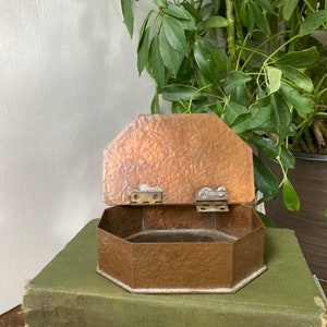 May include: An octagonal copper box with a hammered finish and a hinged lid. The box is open and sitting on a stack of books.