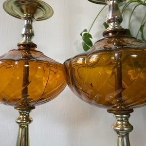 May include: A pair of amber glass table lamps with gold and silver accents. The lamps have a unique, textured design and are perfect for adding a touch of vintage style to any room.