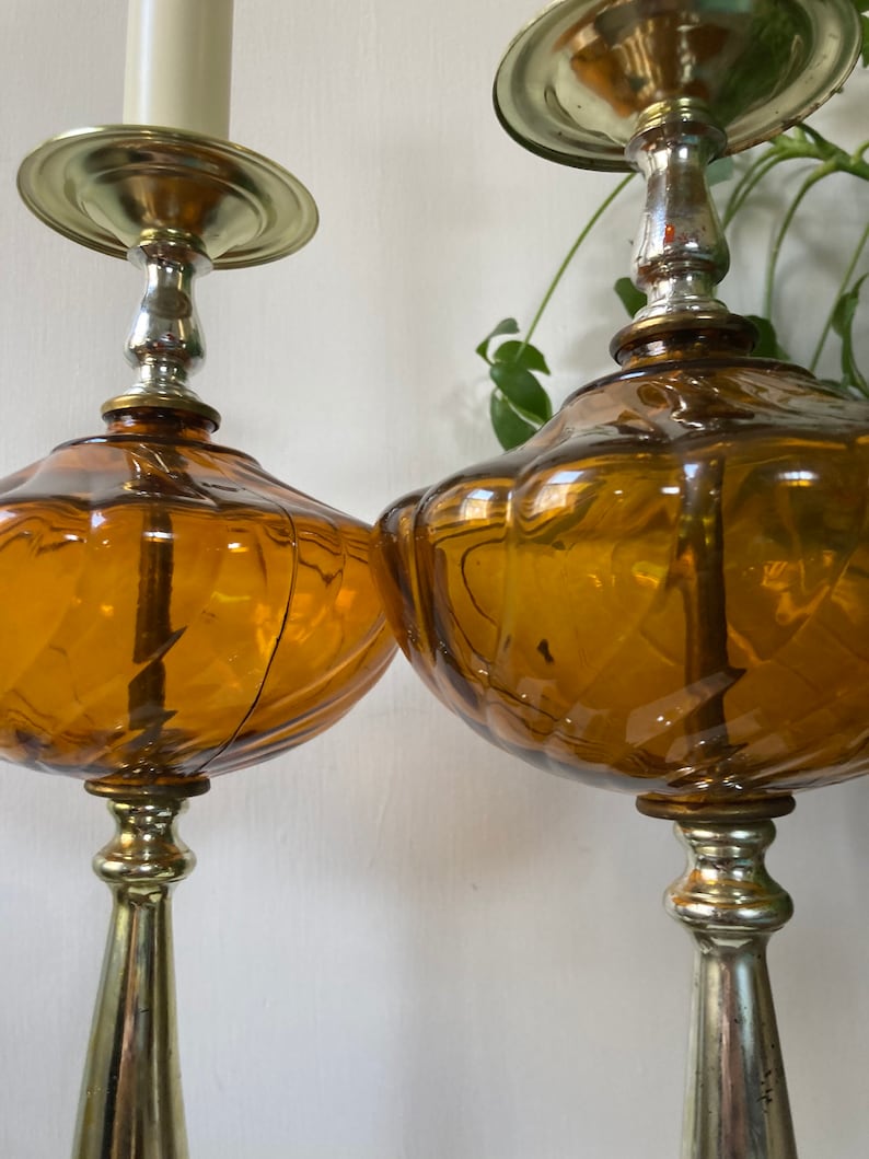 May include: A pair of amber glass table lamps with gold and silver accents. The lamps have a unique, textured design and are perfect for adding a touch of vintage style to any room.