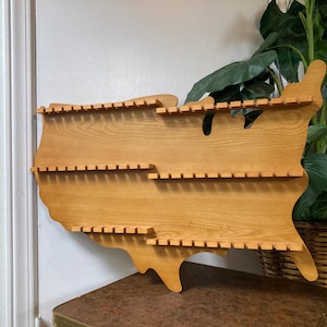 May include: Wooden wall shelf shaped like the United States of America with multiple shelves for displaying items.
