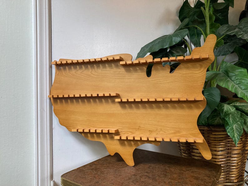 May include: Wooden wall shelf shaped like the United States of America with multiple shelves for displaying items.