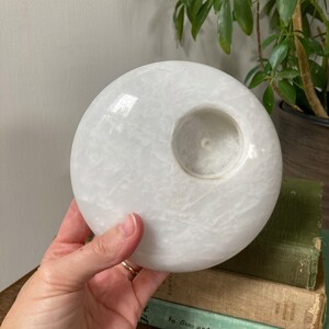 May include: White round candle holder made of marble with a circular opening in the centre for a candle.
