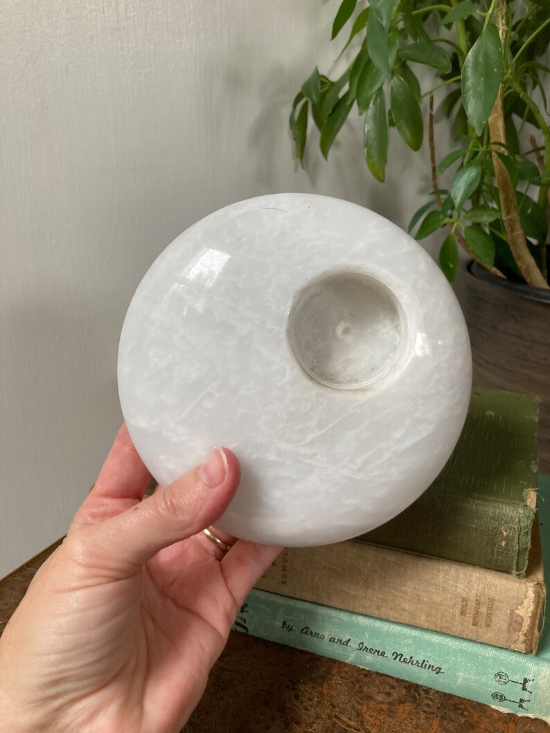 May include: White round candle holder made of marble with a circular opening in the centre for a candle.