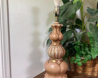 May include: A ceramic table lamp with a brown and gold base. The base has a textured design and a bulbous shape. The lamp is sitting on a brown table.