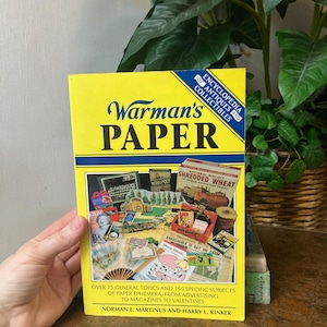 May include: A yellow book titled "Warman's Paper" with blue and black text. The book cover features a collage of vintage paper ephemera, including advertisements and magazines. The book is an encyclopedia of antiques and collectibles.