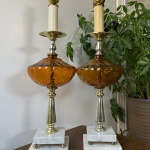 May include: A pair of amber glass table lamps with white marble bases. The lamps have a gold-tone finish and a swirl design on the glass.