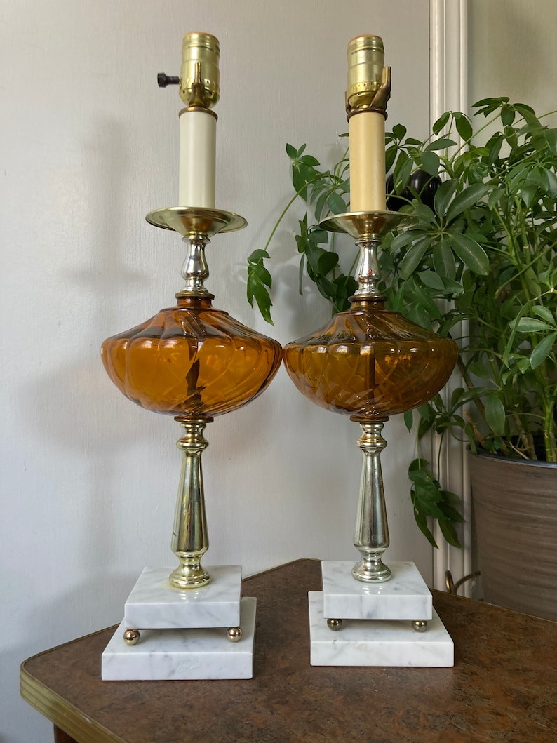 May include: A pair of amber glass table lamps with white marble bases. The lamps have a gold-tone finish and a swirl design on the glass.
