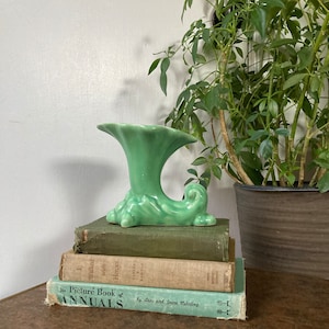 May include: A green ceramic vase with a unique, wave-like design. The vase is sitting on a stack of vintage books with the title "The Picture Book of Annuals" visible.