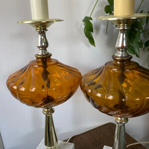 May include: A pair of amber glass table lamps with white marble bases and gold accents. The lamps have a fluted design and are topped with a candle-style bulb.