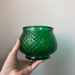 May include: A green glass vase with a textured, scale-like pattern. The vase has a rounded body and a wide base.