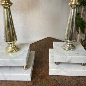 May include: Two marble and metal candle holders with a swirl pattern on the top. The candle holders are on a brown surface.