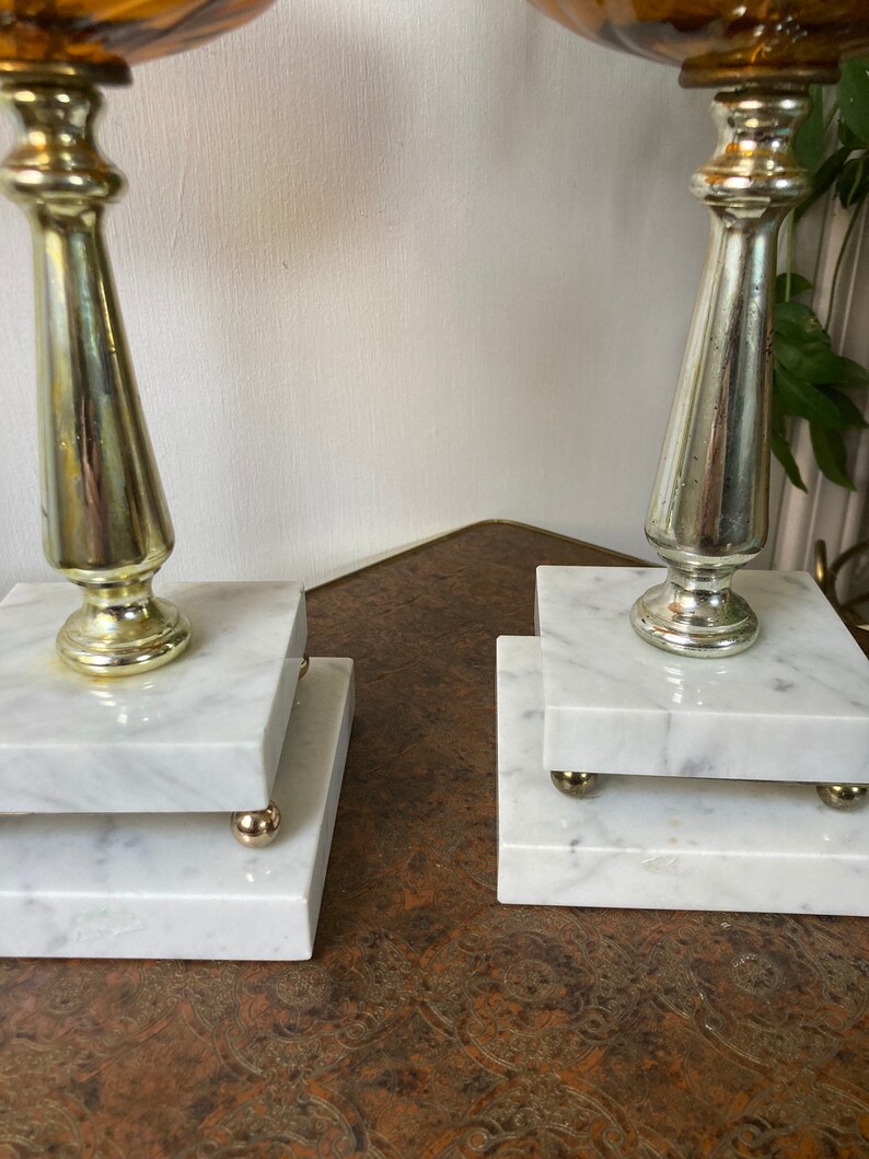 May include: Two marble and metal candle holders with a swirl pattern on the top. The candle holders are on a brown surface.