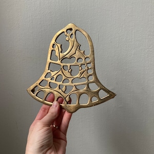 May include: A gold-colored metal bell ornament with a cut-out design of holly leaves and berries.