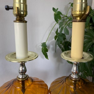 May include: A pair of amber glass table lamps with a scalloped design. The lamps have a brass base and a white ceramic shade.