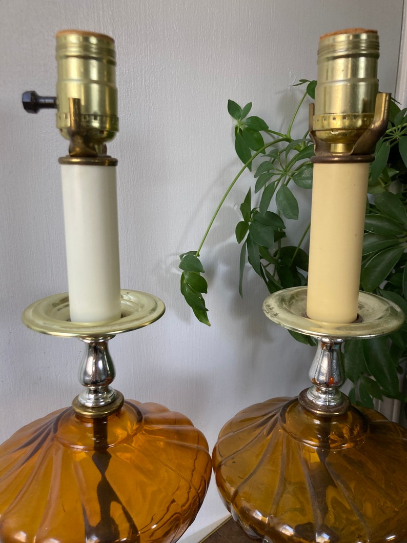May include: A pair of amber glass table lamps with a scalloped design. The lamps have a brass base and a white ceramic shade.