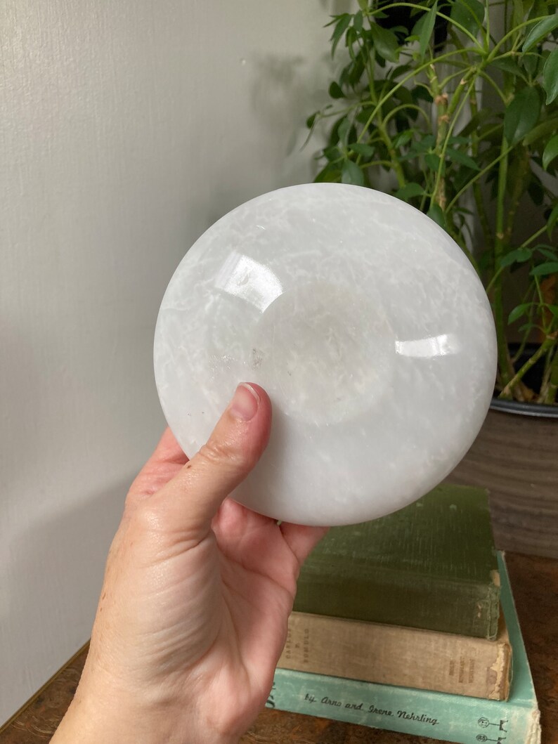May include: A white selenite disc, also known as a selenite plate, is a smooth, round, and polished piece of selenite crystal. It has a white, opaque appearance with subtle striations and a slightly translucent quality.