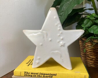 May include: White ceramic star-shaped decorative object with a textured surface and a subtle embossed design. The star is sitting on top of a stack of three books with titles related to gardening and flowers.