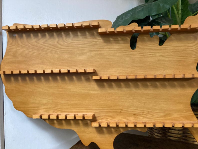 May include: Wooden wall shelf shaped like the United States of America with three rows of slots for displaying items.