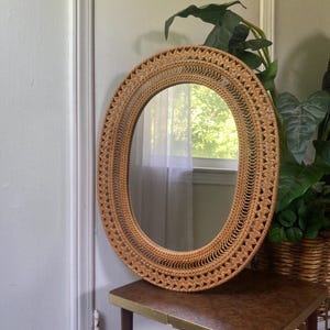 May include: A round mirror featuring a light brown woven rattan frame with an intricate, repeating open-work pattern. The frame consists of a textured outer border and a delicate inner ring of vertical spokes surrounding the central glass surface.