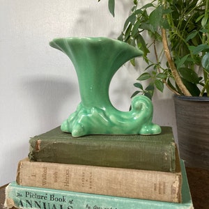 May include: A green ceramic vase with a unique, wave-like design. The vase is sitting on top of a stack of three books.