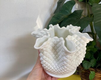May include: A white milk glass vase with a ruffled top and a diamond pattern. The vase is held in a hand.