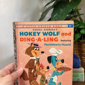 May include: Vintage "Hokey Wolf and Ding-A-Ling" Little Golden Book. The cover features cartoon illustrations of Hokey Wolf, Ding-A-Ling, and Huckleberry Hound. The book has a pink cover with blue and red text. The book is held by a hand.