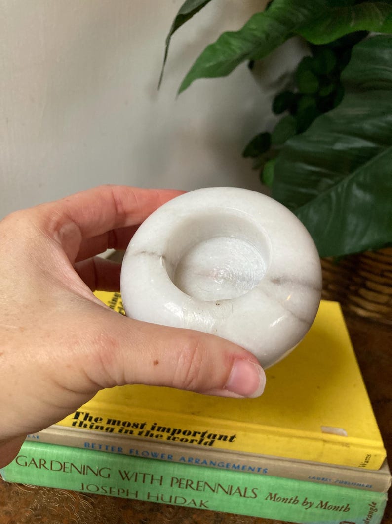 May include: White marble candle holder with a round, slightly indented top. The holder is smooth and has a subtle gray veining.