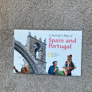 May include: A Traveler's Map of Spain and Portugal from the National Geographic Society. The cover features a stone archway, illustrations of people in traditional clothing, and the title in red and white text.