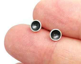 May include: A pair of small, round, black and silver stud earrings. The earrings are made of metal and have a smooth, polished finish.